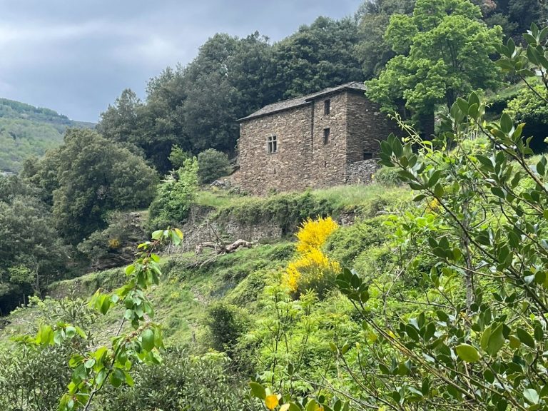 Une ancienne maison en pierre entourée de verdure et de collines.